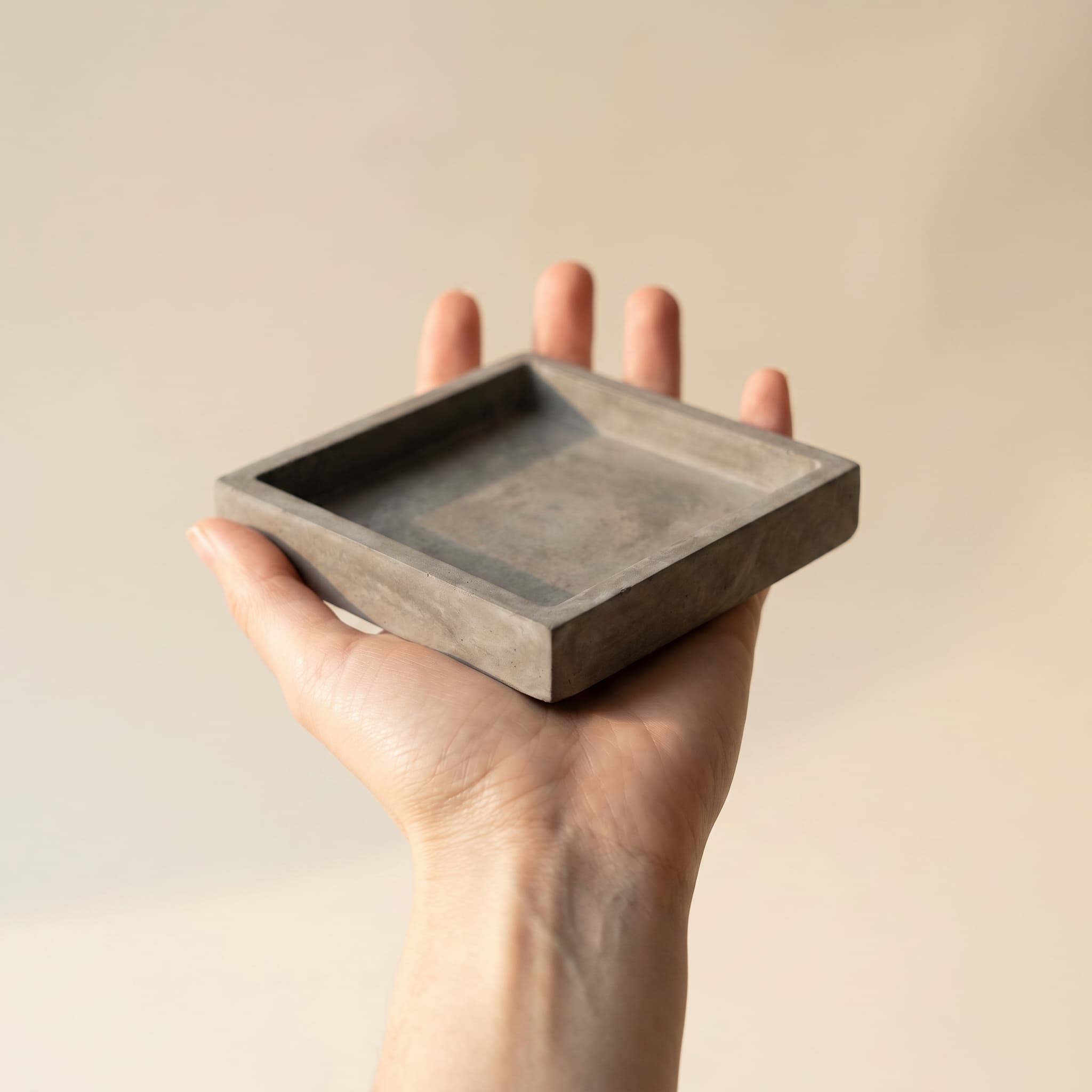 Square grey saucer held in a hand